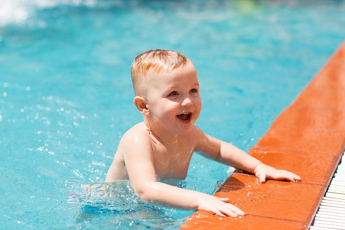 Un bébé tout sourire dans l'eau d'une piscine se tenant au rebord