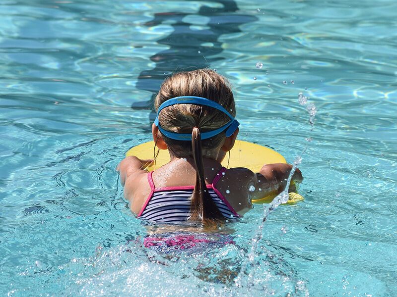 Une fille qui nage dans une piscine à l'aide d'une planche de natation