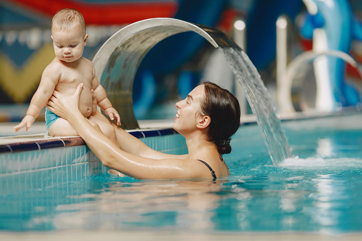 Une maman qui tient son fils par les bras sur le rebord d'une piscine