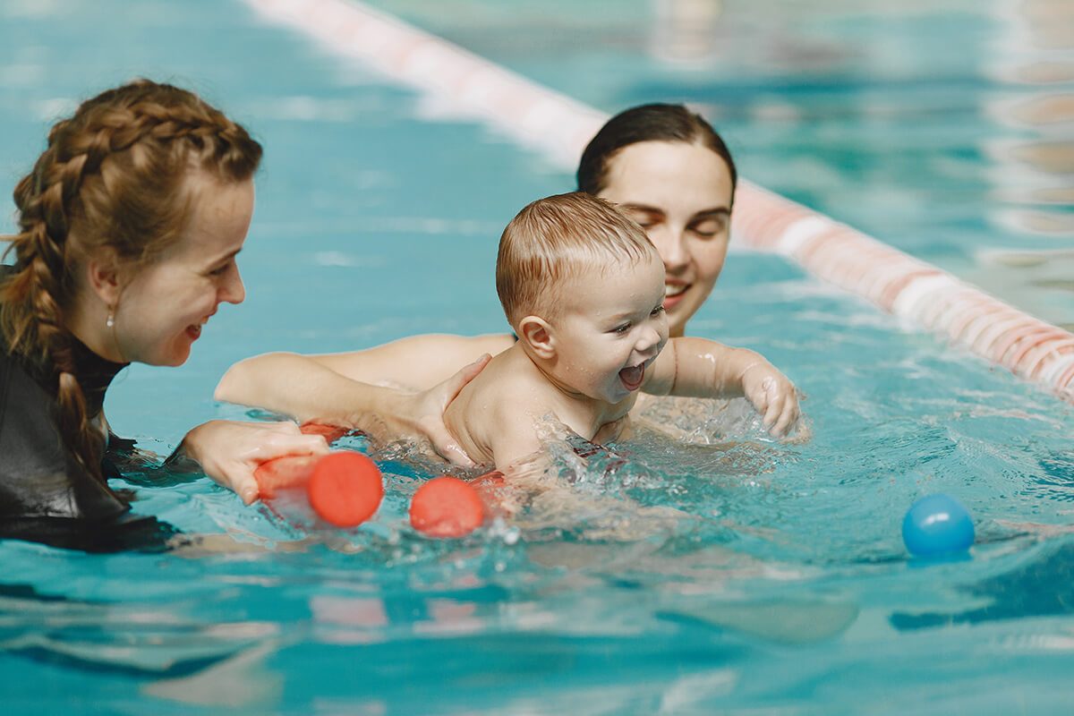 Un bébé avec sa maman et une maitre-nageur à la piscine