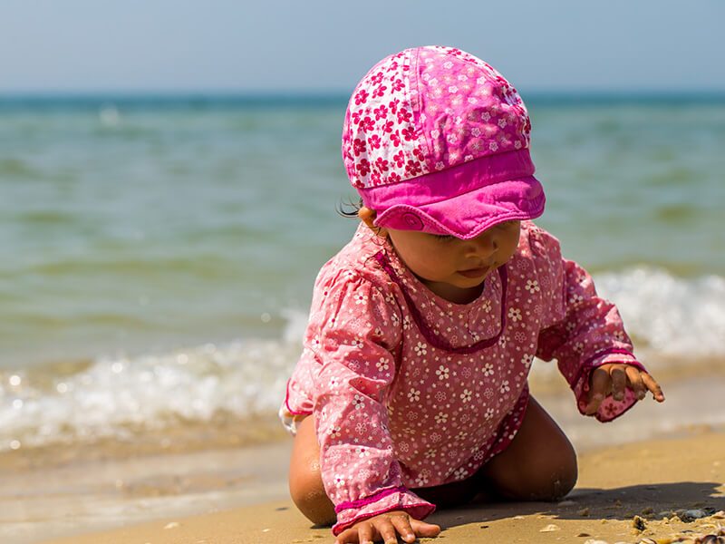 Un bébé au bord de l'eau à la plage qui porte un chapeau