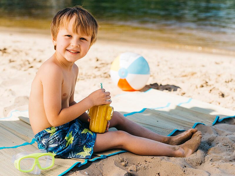 Un enfant assis sur la plage avec une boisson à la main
