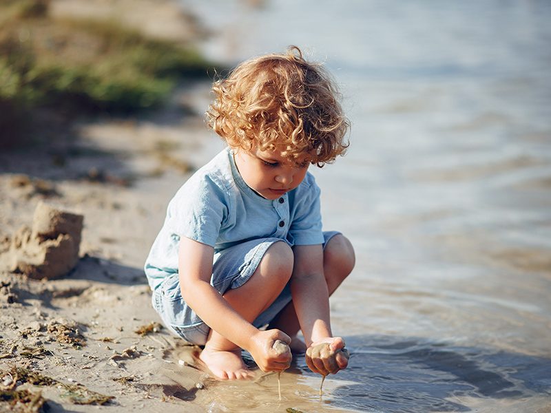 Un bébé à la plage qui joue avec le sable au bord de l'eau