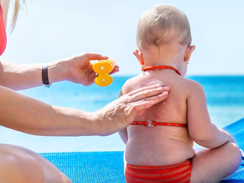 Une maman qui met de la crème solaire à son bébé à la plage