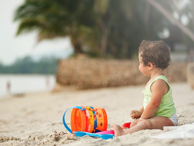 Un bébé avec un seau et un rateau assis sur la plage