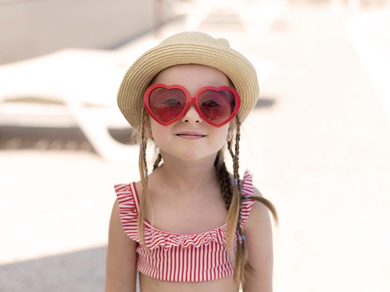 Un bébé à la plage qui porte un chapeau et des lunettes de soleil
