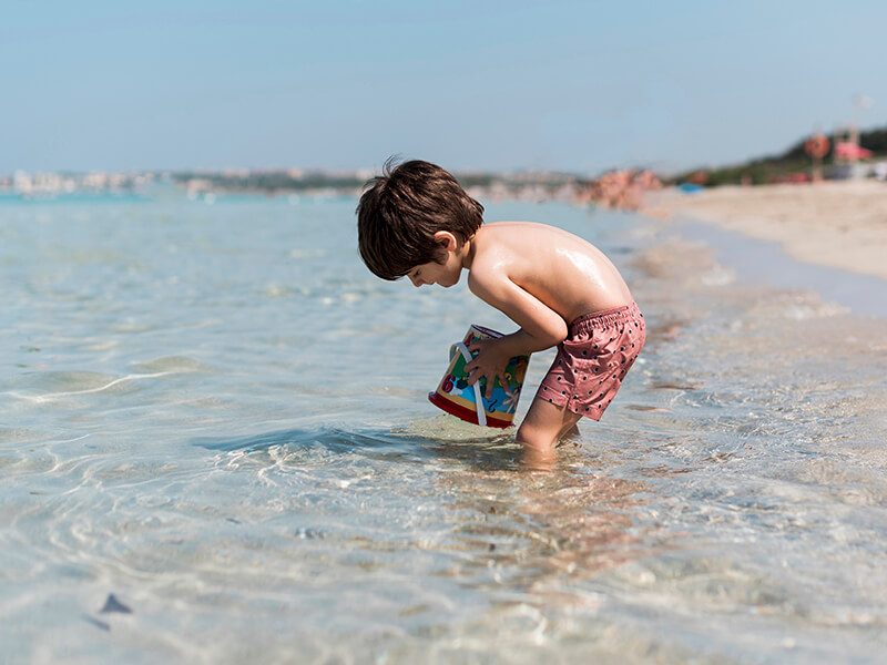 Un bébé en maillot de bain avec les pieds dans l'eau à la plage