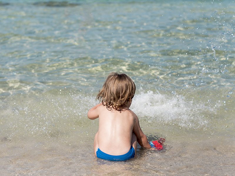 Un bébé à la plage assis sur le sable au bord de l'eau