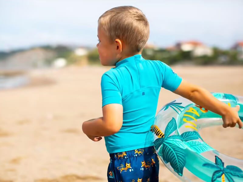 Un bébé qui porte un t-shirt anti-UV à la plage