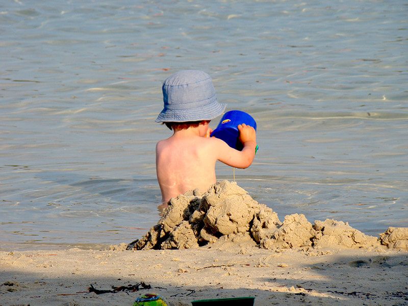 Un bébé avec un chapeau de dos qui joue avec le sable à la plage