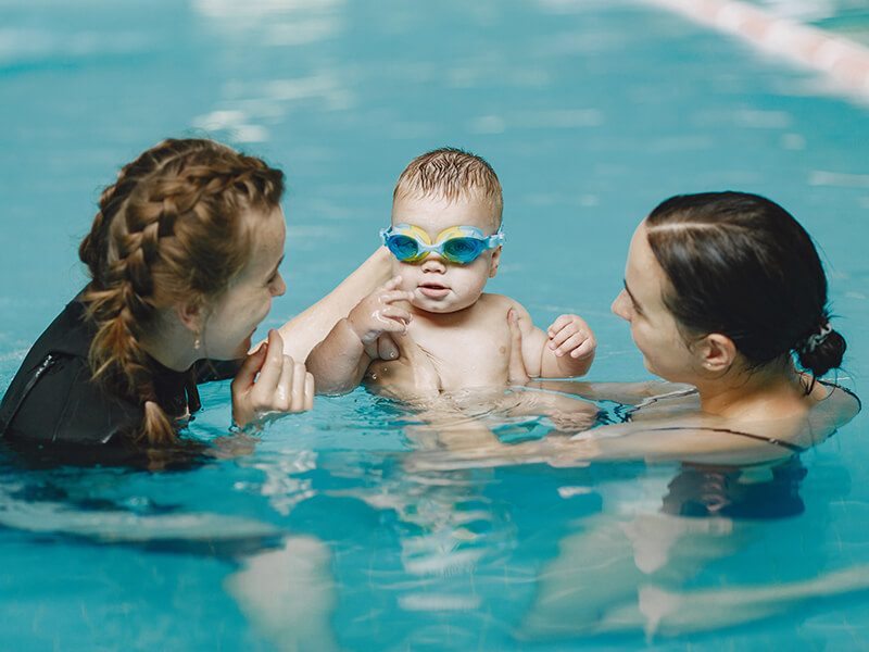 Un bébé autour de sa maman et d'une maître-nageuse dans le bassin d'une piscine