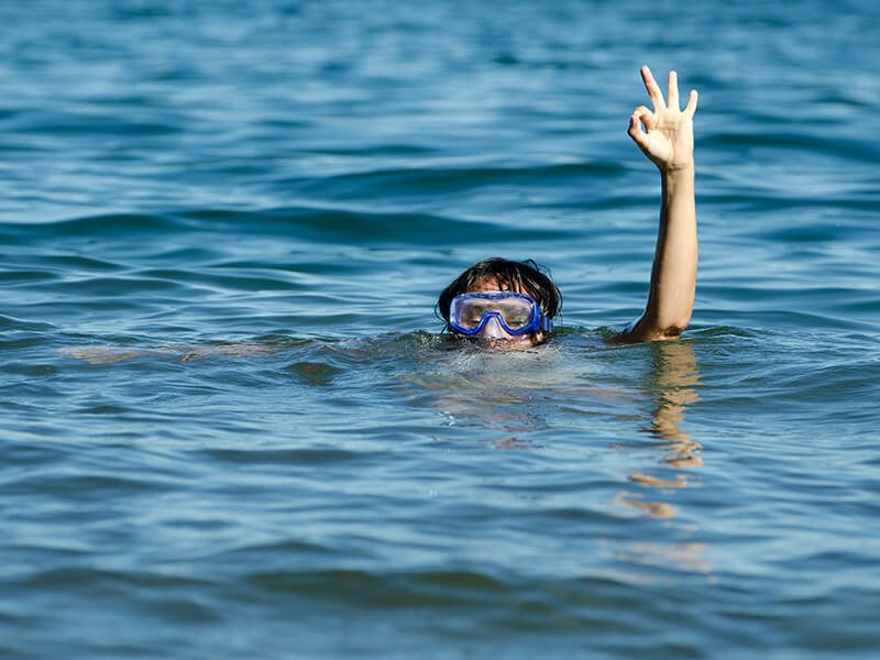 Une enfant qui fait un signe de la main hors de l'eau pendant sa sortie snorkeling