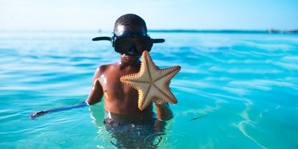 Un enfant dans l'eau avec une étoile de mer dans les mains après avoir fait du snorkeling