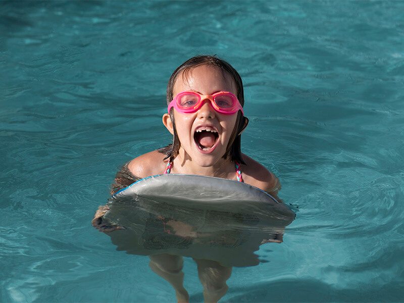 Une enfant qui sourit avec ses lunettes de piscine dans un bassin