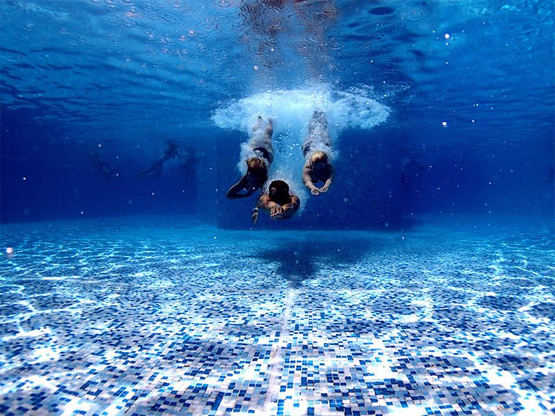 Trois personnes qui plongent sous l'eau dans une piscine