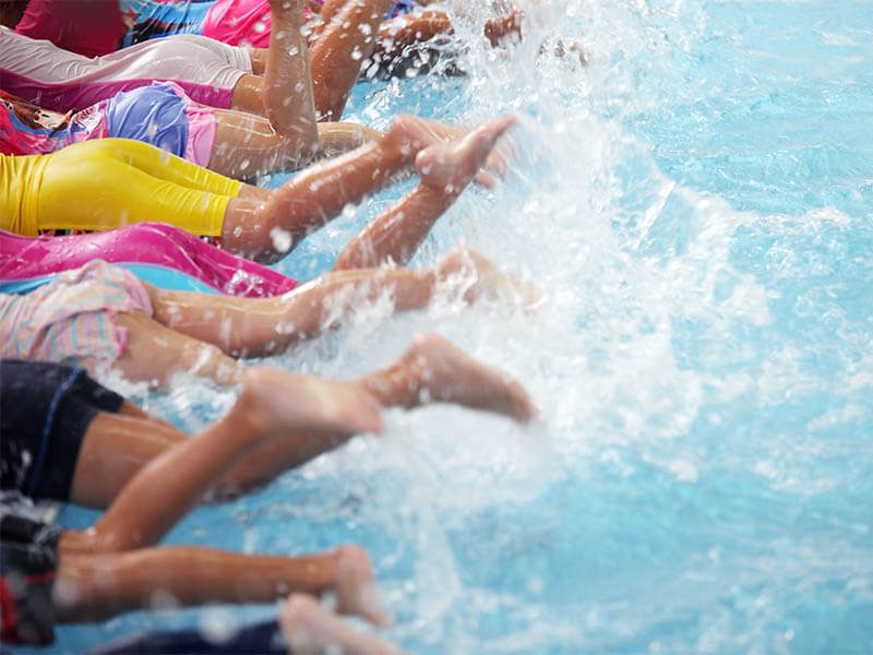 Des enfants qui battent des pieds lors de leur leçon de piscine avec l'école