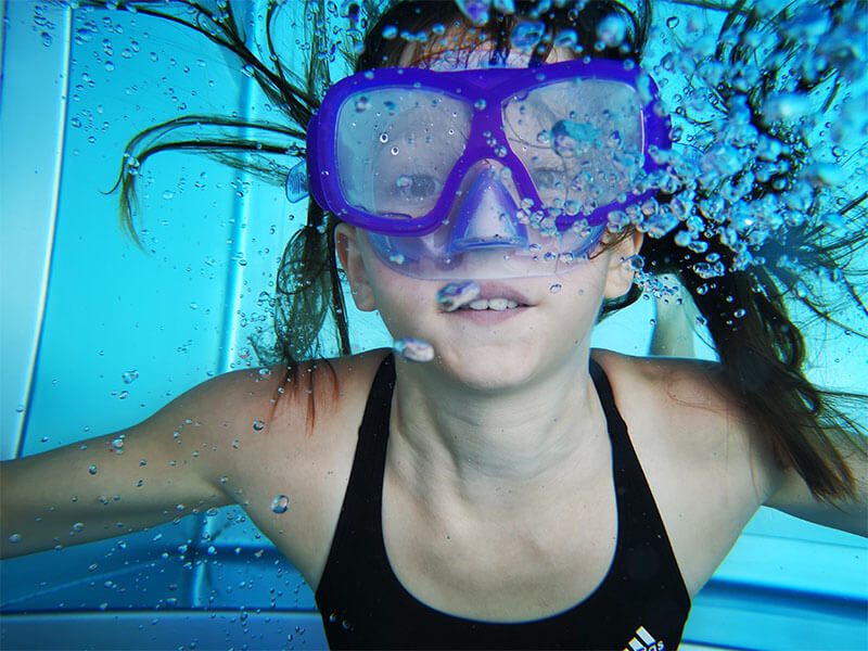 Une enfant la tête sous l'eau avec un masque de natation sur le visage