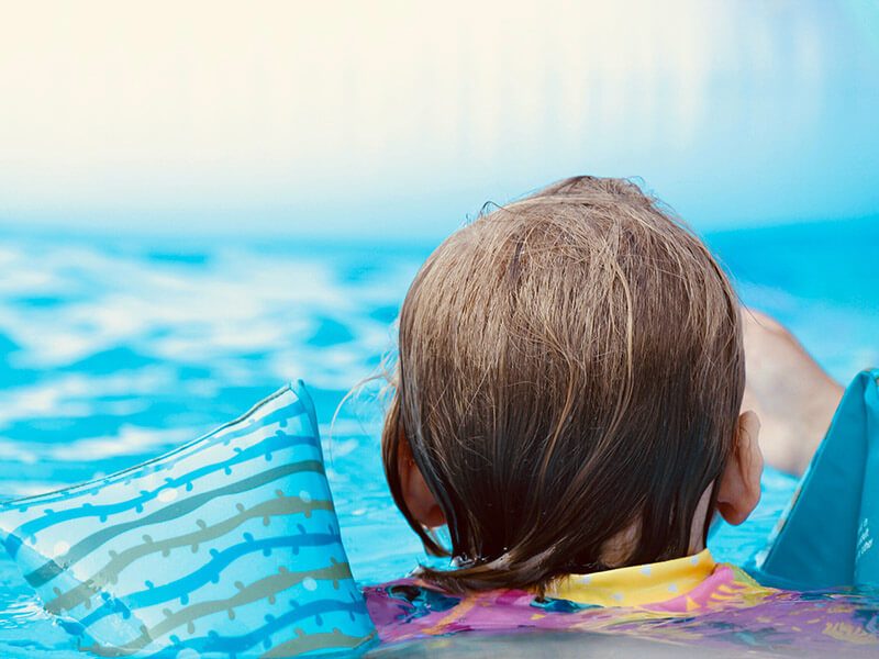Un enfant avec des brassards de dos dans l'eau