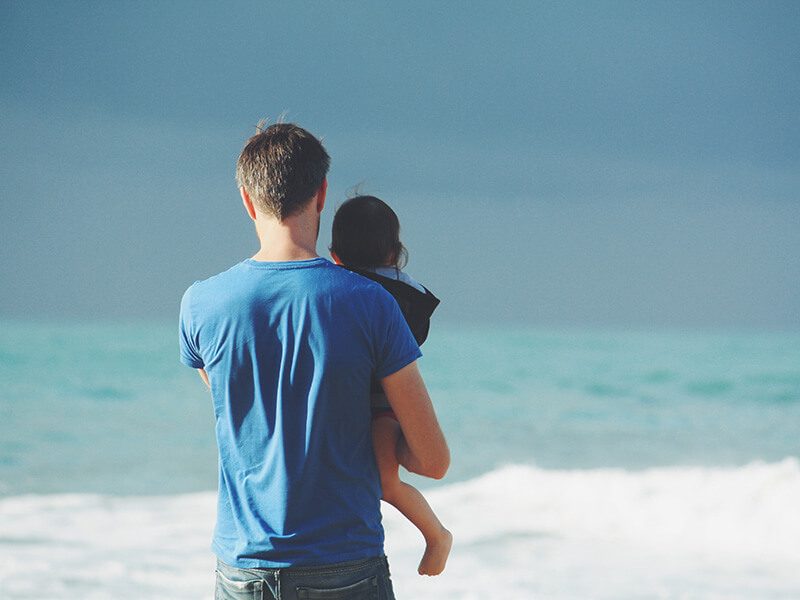 Un père avec son enfant dans les bras devant la mer