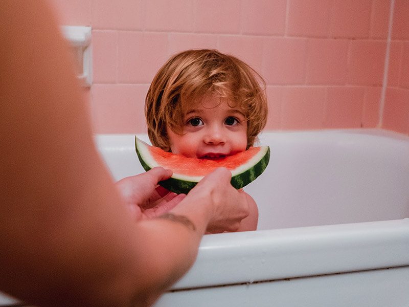 Un enfant qui mange un morceau de pastèque pendant son bain
